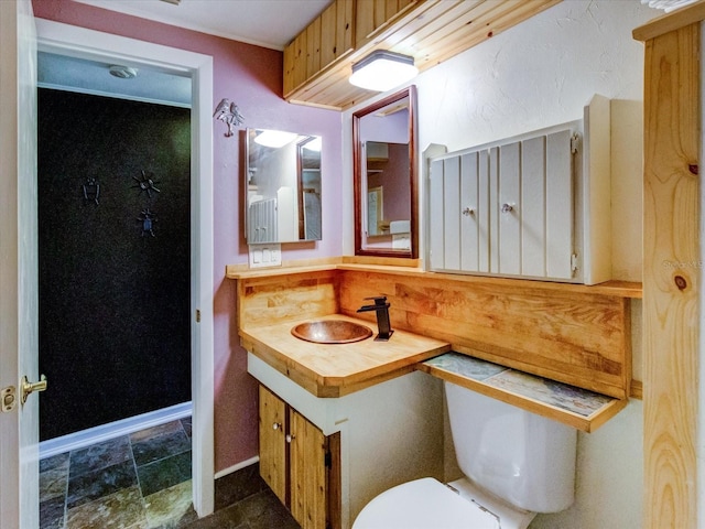 half bathroom featuring stone finish flooring, vanity, toilet, and baseboards