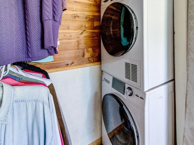 clothes washing area featuring stacked washer and dryer, wood walls, and laundry area