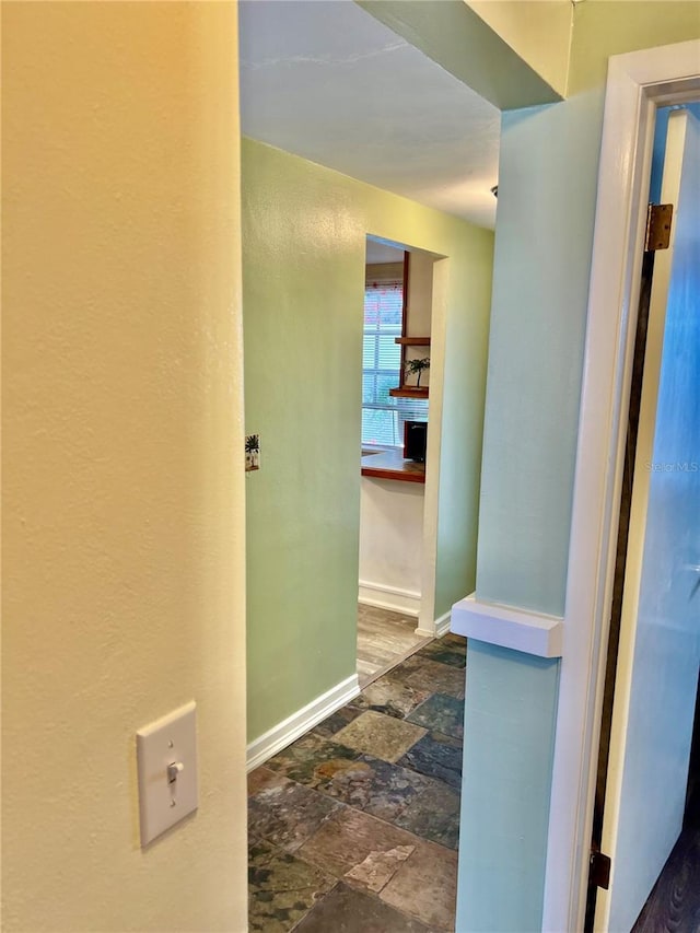 hall with stone tile flooring and baseboards