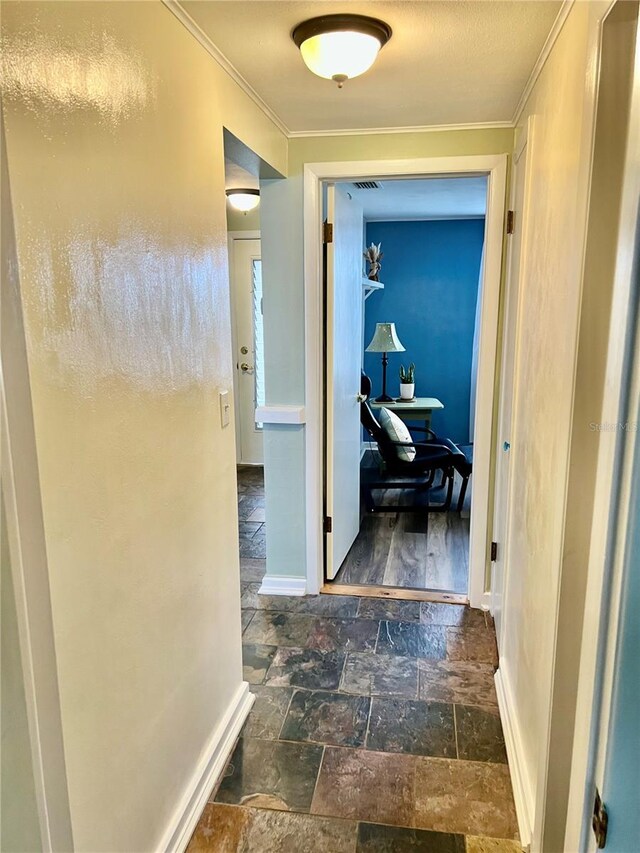 hall featuring visible vents, ornamental molding, stone tile flooring, and baseboards