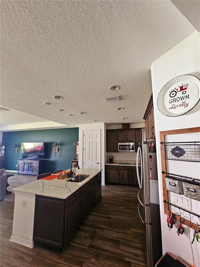 kitchen featuring appliances with stainless steel finishes, an island with sink, sink, light stone countertops, and dark brown cabinets