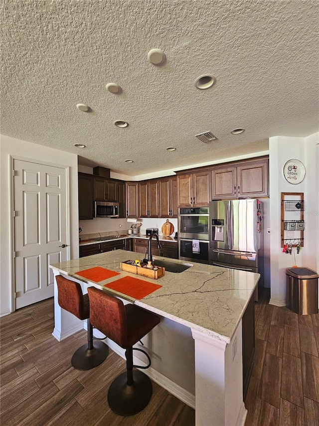 kitchen with light stone counters, sink, a center island with sink, and appliances with stainless steel finishes