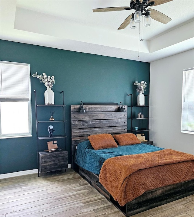 bedroom featuring ceiling fan, a raised ceiling, and light wood-type flooring