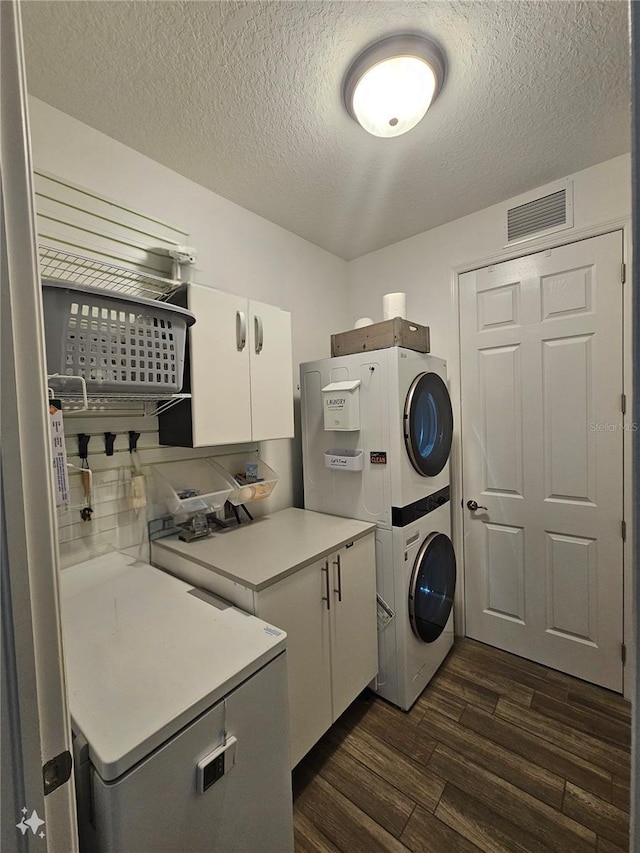 clothes washing area with dark hardwood / wood-style floors, cabinets, a textured ceiling, and stacked washer / dryer