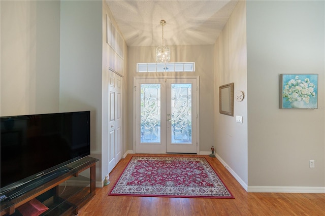 foyer featuring wood-type flooring, french doors, and a chandelier