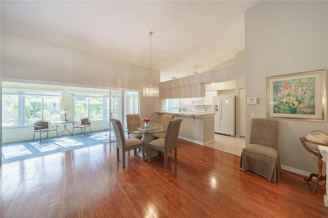 dining room featuring light wood finished floors, baseboards, high vaulted ceiling, and an inviting chandelier