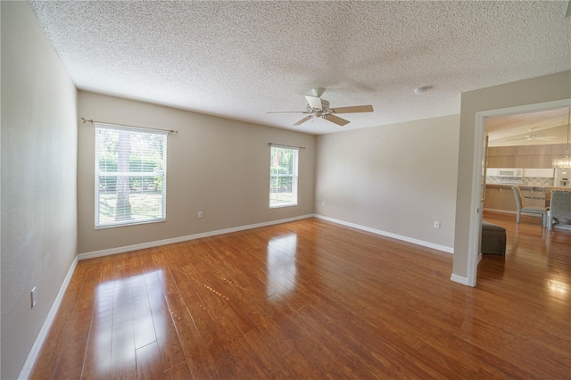 empty room with a ceiling fan, a textured ceiling, baseboards, and wood finished floors