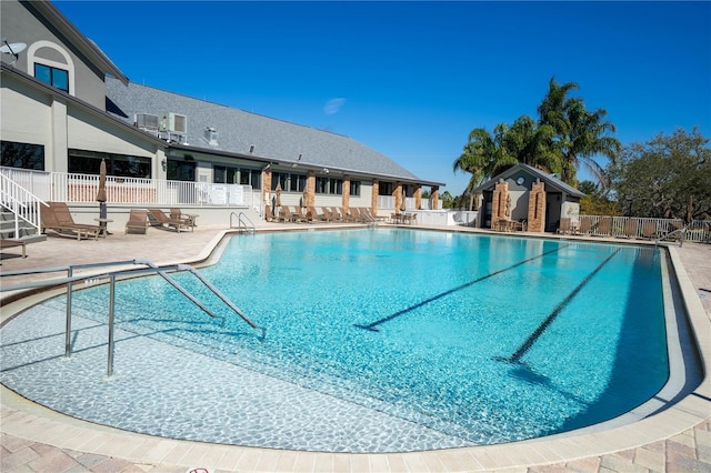 community pool with a patio area, fence, and an outdoor structure