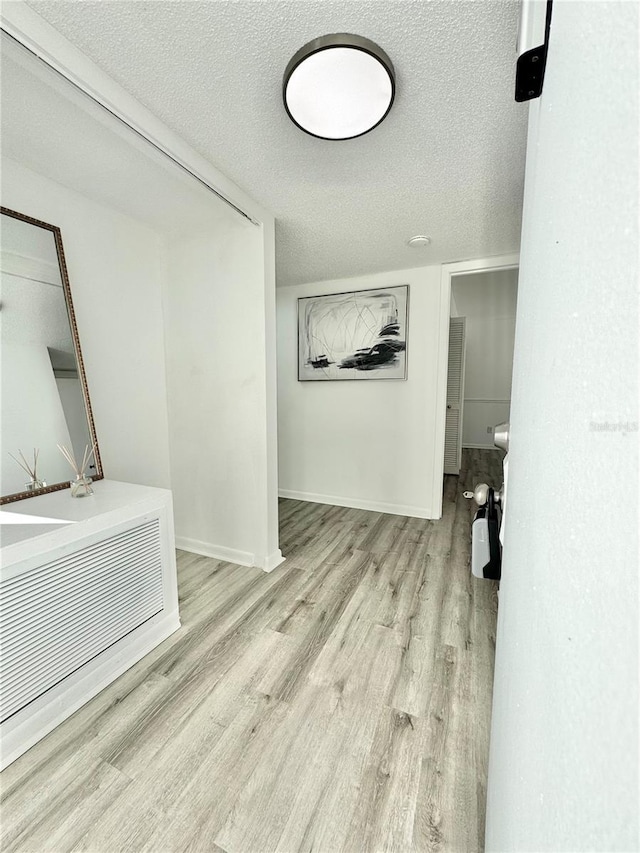 corridor with a textured ceiling, light wood-type flooring, and baseboards