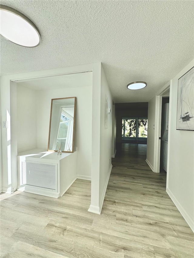 hallway with light wood-type flooring, plenty of natural light, baseboards, and a textured ceiling