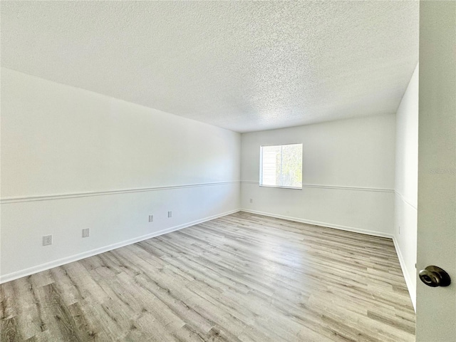 spare room featuring light wood-type flooring, baseboards, and a textured ceiling