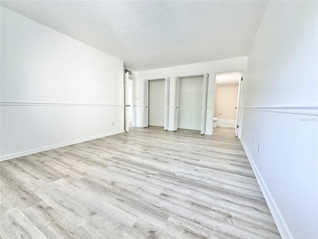 unfurnished bedroom with a textured ceiling, baseboards, multiple closets, light wood finished floors, and ensuite bath