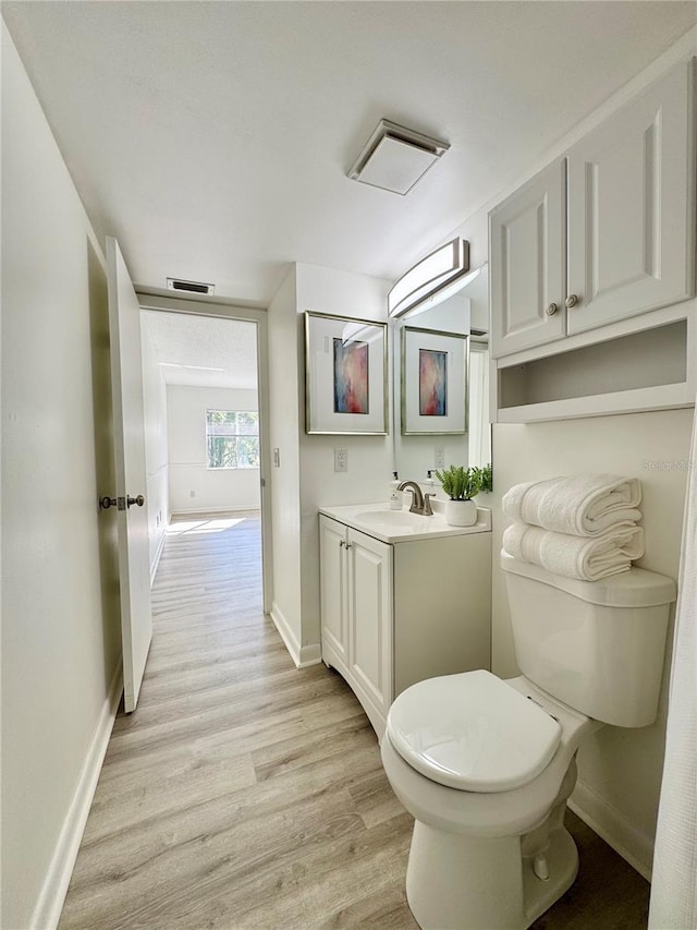 bathroom with visible vents, toilet, vanity, wood finished floors, and baseboards