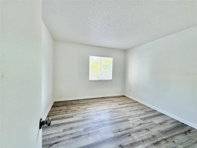 unfurnished room featuring a textured ceiling, light wood-type flooring, and baseboards