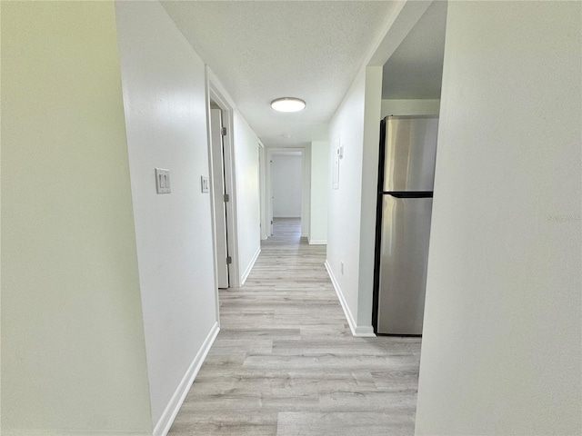 hall featuring a textured ceiling, light wood-type flooring, and baseboards