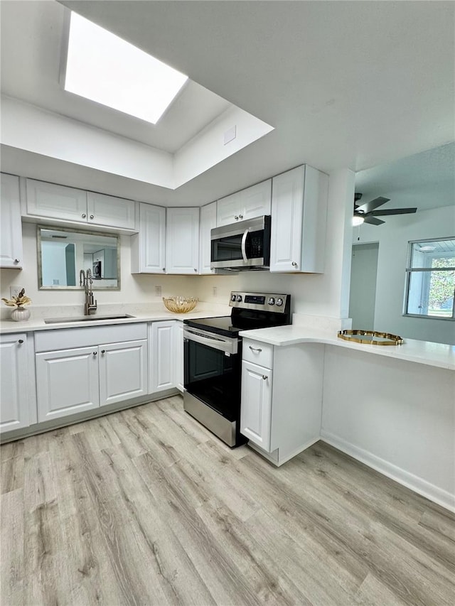 kitchen with stainless steel appliances, a sink, white cabinets, light countertops, and light wood finished floors