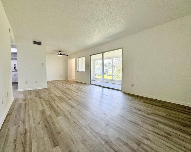 empty room featuring light wood-type flooring, ceiling fan, visible vents, and a textured ceiling