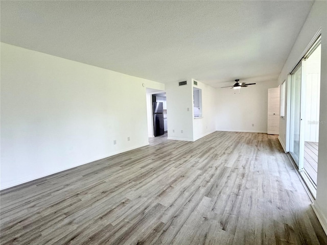 empty room featuring visible vents, ceiling fan, a textured ceiling, light wood-type flooring, and baseboards