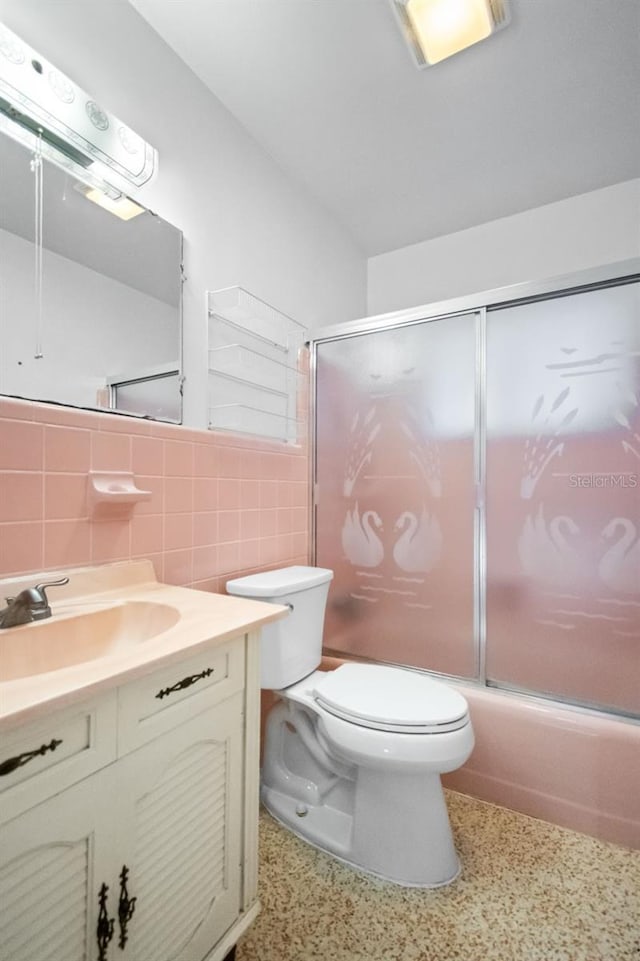 full bathroom with combined bath / shower with glass door, tile walls, vanity, decorative backsplash, and toilet