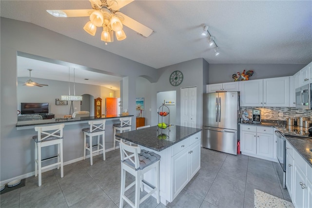 kitchen featuring vaulted ceiling, appliances with stainless steel finishes, a breakfast bar, white cabinets, and backsplash