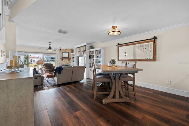 dining room with crown molding, a stone fireplace, dark hardwood / wood-style floors, and ceiling fan