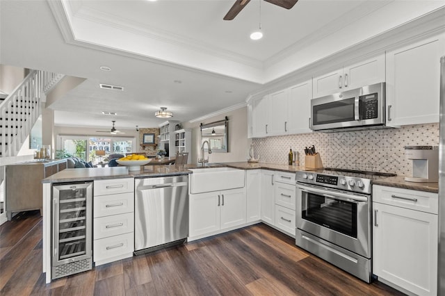 kitchen with wine cooler, sink, appliances with stainless steel finishes, kitchen peninsula, and white cabinets