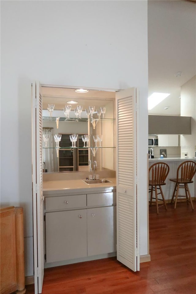 bar with wood-type flooring, sink, and white cabinets