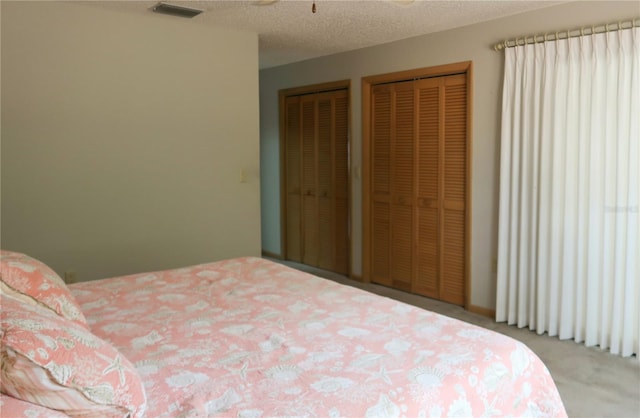 carpeted bedroom featuring two closets and a textured ceiling