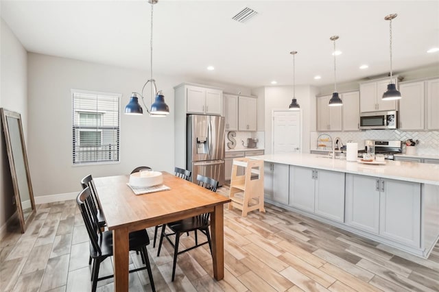 kitchen featuring pendant lighting, backsplash, light wood-type flooring, and appliances with stainless steel finishes