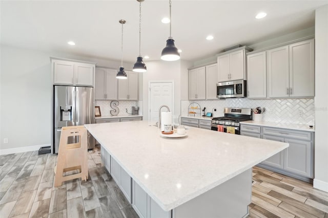 kitchen featuring pendant lighting, stainless steel appliances, a center island with sink, and backsplash