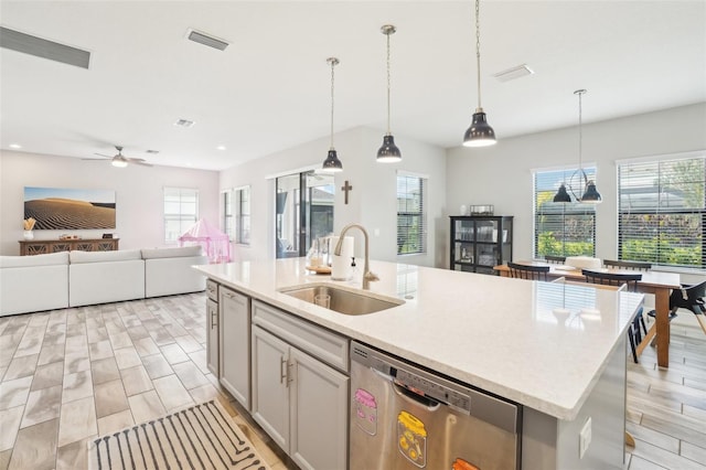 kitchen with dishwasher, an island with sink, sink, hanging light fixtures, and light hardwood / wood-style flooring