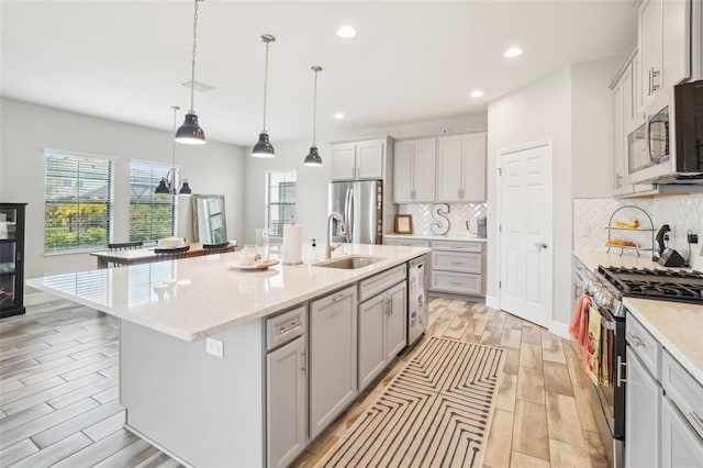 kitchen with appliances with stainless steel finishes, sink, decorative backsplash, hanging light fixtures, and a kitchen island with sink