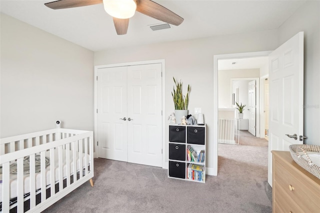 bedroom featuring a crib, carpet flooring, ceiling fan, and a closet