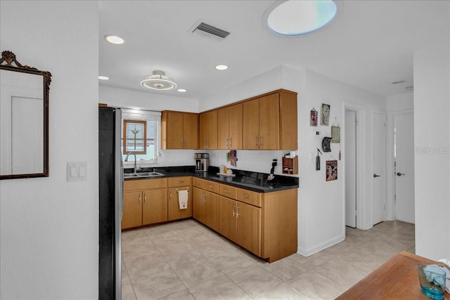 kitchen featuring a sink, dark countertops, visible vents, brown cabinets, and light tile patterned floors