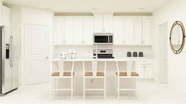 kitchen featuring light tile patterned flooring, white cabinetry, a center island with sink, a kitchen breakfast bar, and stainless steel appliances