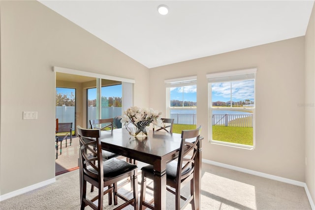 dining space with vaulted ceiling, light colored carpet, and a water view