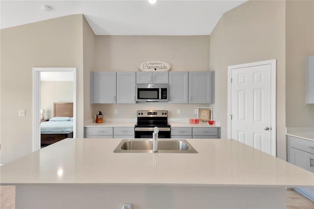 kitchen featuring stainless steel appliances, sink, a center island with sink, and gray cabinets