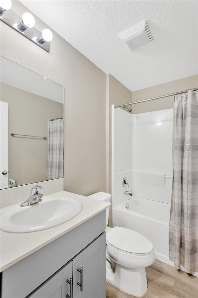 full bathroom with shower / tub combo, hardwood / wood-style floors, vanity, a textured ceiling, and toilet