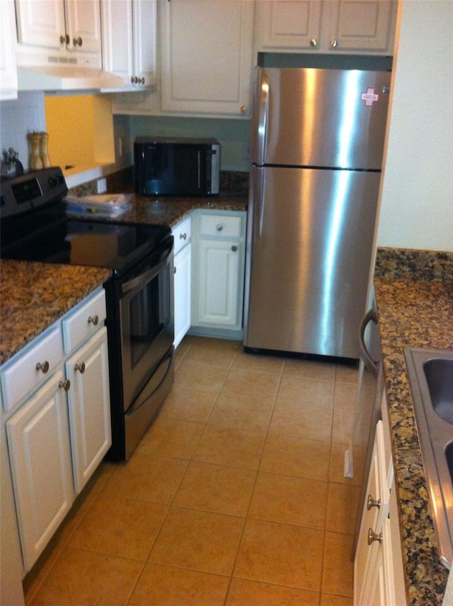 kitchen featuring stainless steel appliances, dark stone countertops, light tile patterned floors, and white cabinets