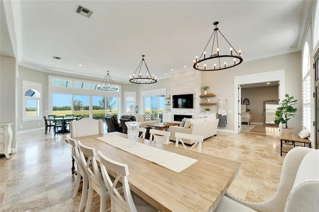 dining space with crown molding, a large fireplace, and a notable chandelier