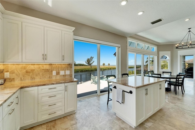 kitchen with white cabinetry, a water view, tasteful backsplash, decorative light fixtures, and light stone countertops