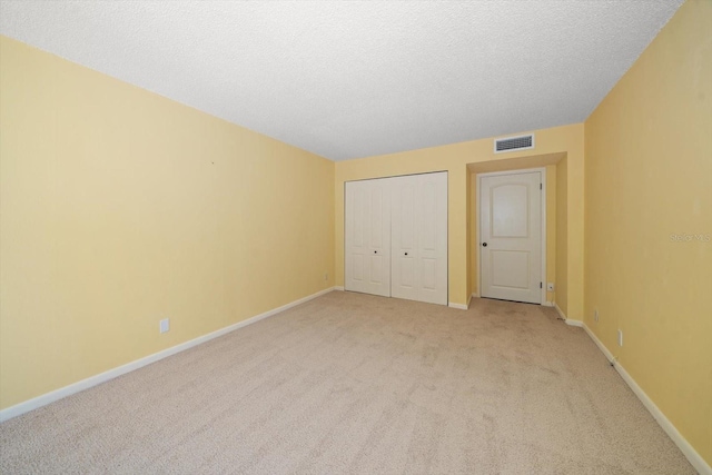 unfurnished bedroom with light carpet, a textured ceiling, and a closet