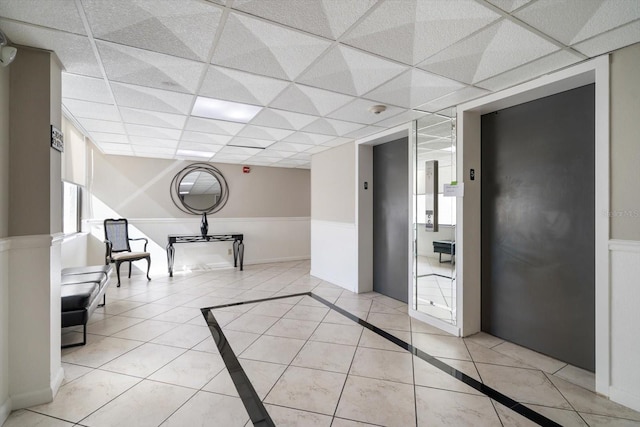 corridor with a drop ceiling, light tile patterned floors, and elevator