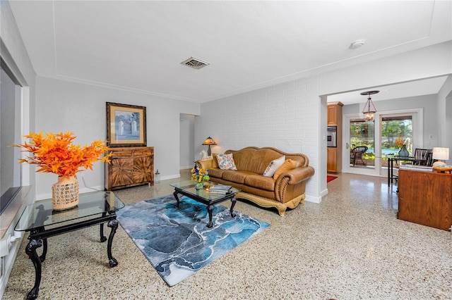 living area with light speckled floor, brick wall, visible vents, and baseboards