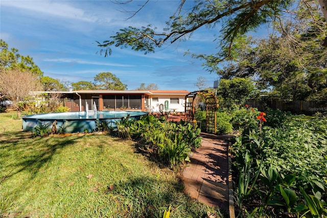 back of property featuring a lawn, fence, a sunroom, and an outdoor pool