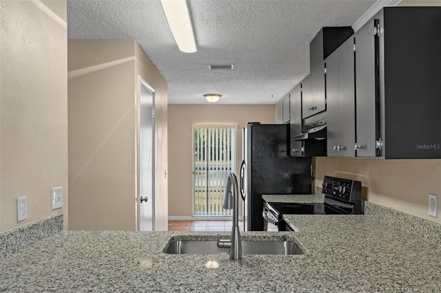 kitchen featuring sink, a textured ceiling, black / electric stove, stainless steel fridge, and light stone countertops