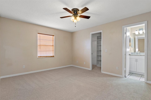 unfurnished bedroom with light carpet, connected bathroom, a spacious closet, and a textured ceiling