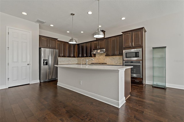 kitchen with pendant lighting, dark wood-type flooring, stainless steel appliances, and an island with sink