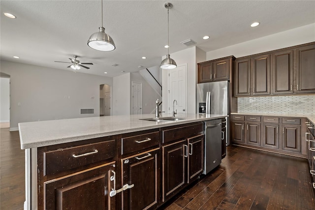 kitchen with dark brown cabinetry, decorative light fixtures, a center island with sink, dark hardwood / wood-style floors, and stainless steel appliances