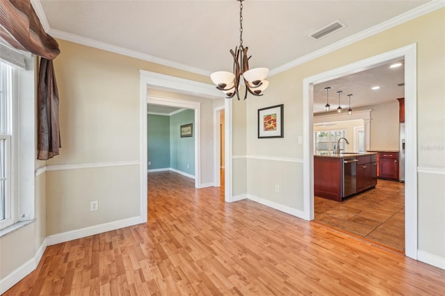 unfurnished dining area featuring sink, ornamental molding, light hardwood / wood-style floors, and a chandelier